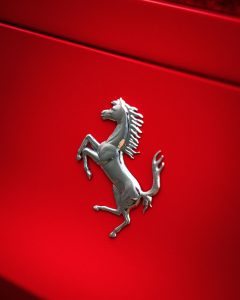 Detailed view of a luxury sports car emblem on a vibrant red vehicle.